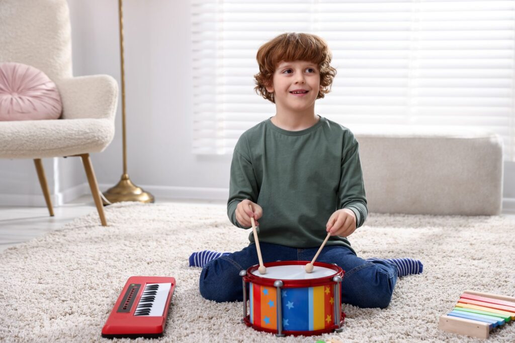 A young boy sits cross-legged playing a colourful toy drum