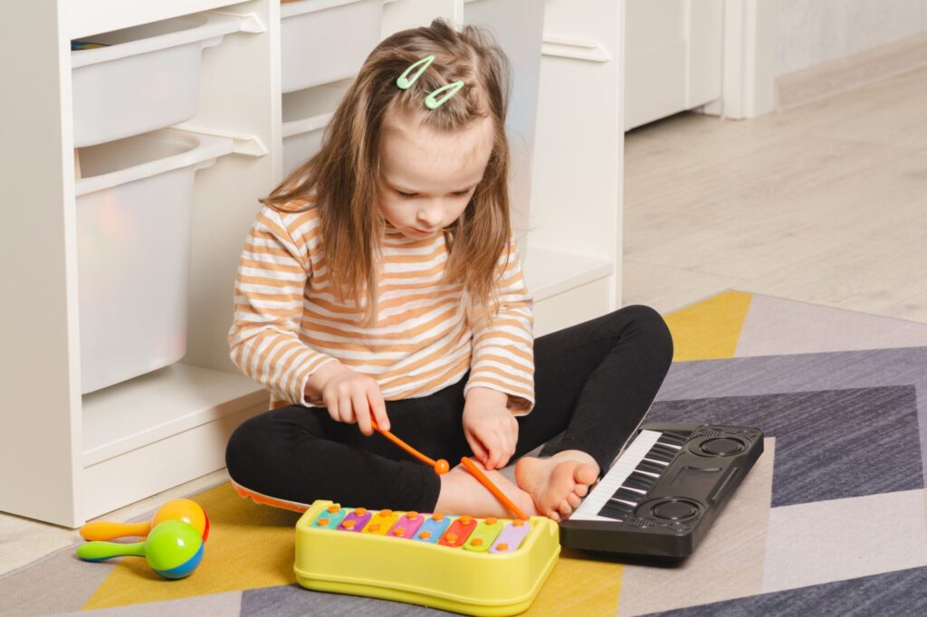 A child sits on the floor playing a toy xylophone and small keyboard