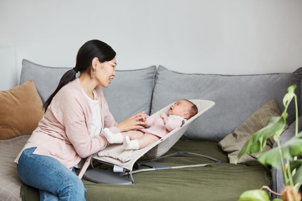 A parent leans in and engages gently with a newborn resting in a bouncer