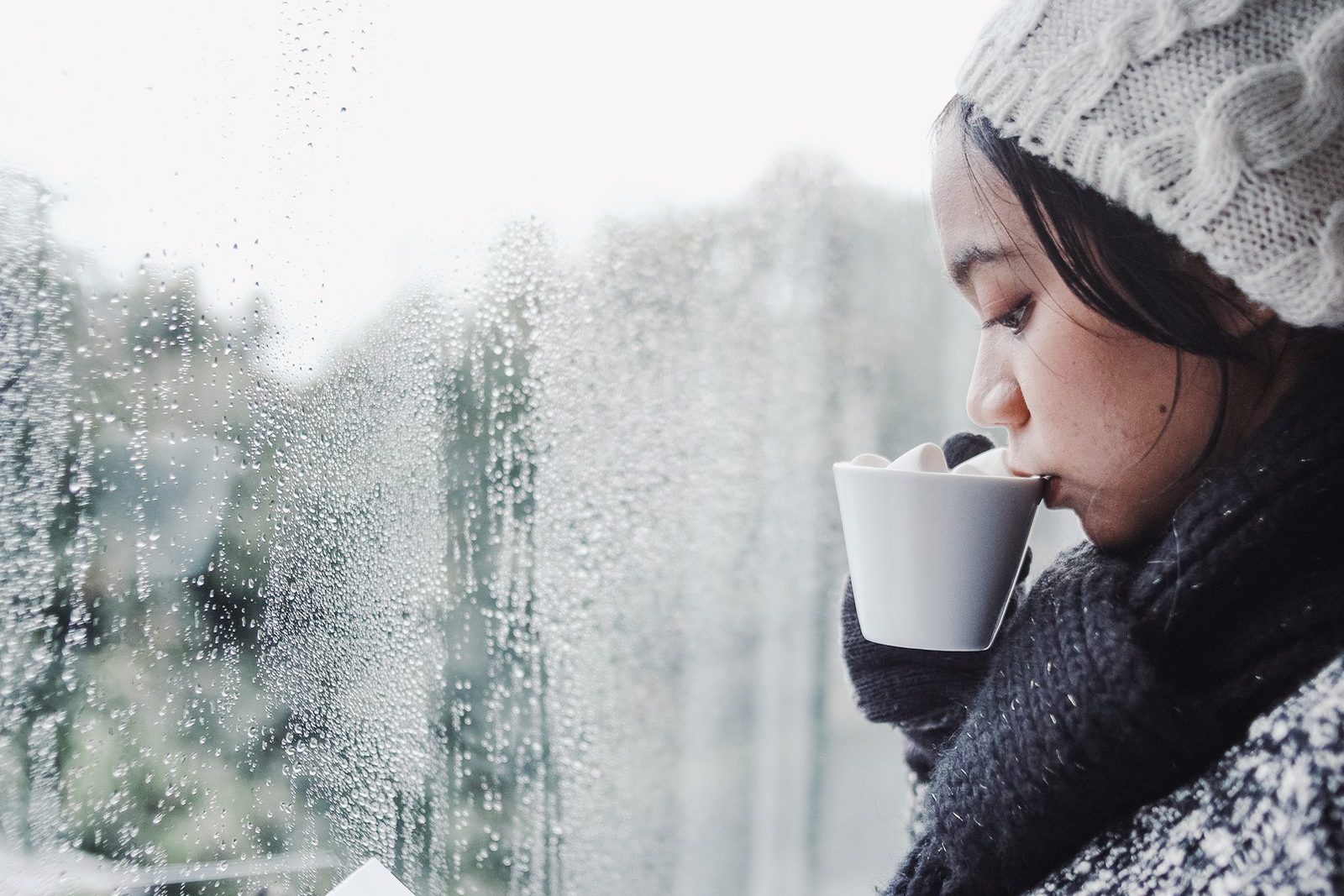 Woman reading with a hot drink by a rainy window